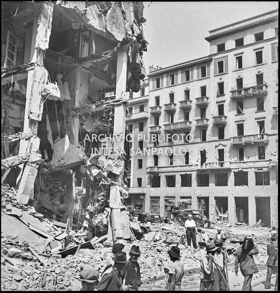 Passanti in via Torino all'angolo con piazza Santa Maria Beltrade, a Milano, davanti a un edificio sventrato dai bombardamenti