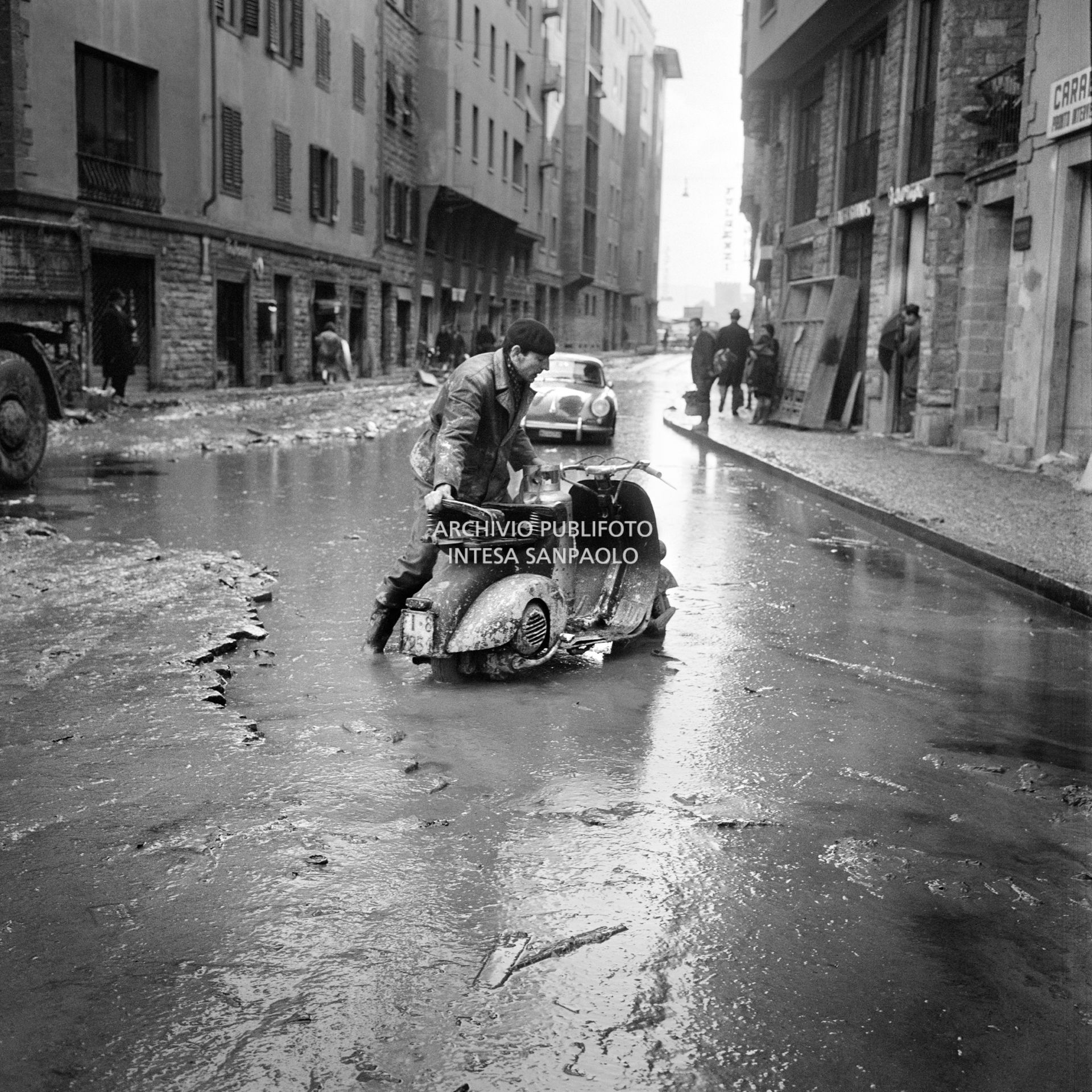 A man pushes a Vespa through the streets of Florence submerged in mud, after the flood