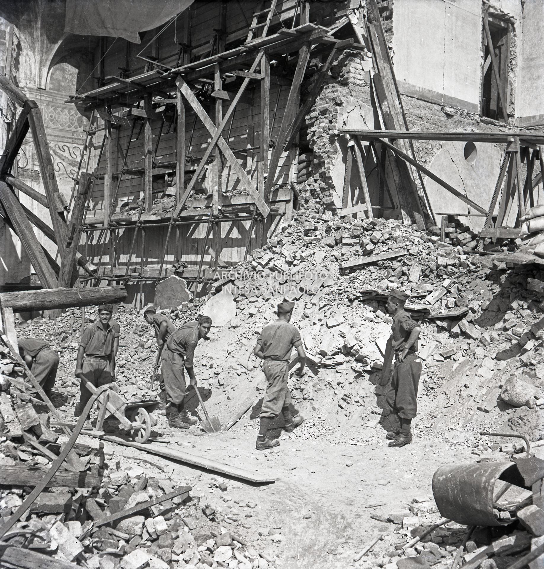 Lavori di rimozione delle macerie della basilica di Santa Maria delle Grazie a Milano dopo i bombardamenti; sullo sfondo sono visibili le impalcature di legno, i sacchi di sabbia, e i rinforzi metallici, su entrambi lati della parete settentrionale del refettorio del convento annesso alla basilica, messi a protezione del Cenacolo vinciano che lo salvaguardarono