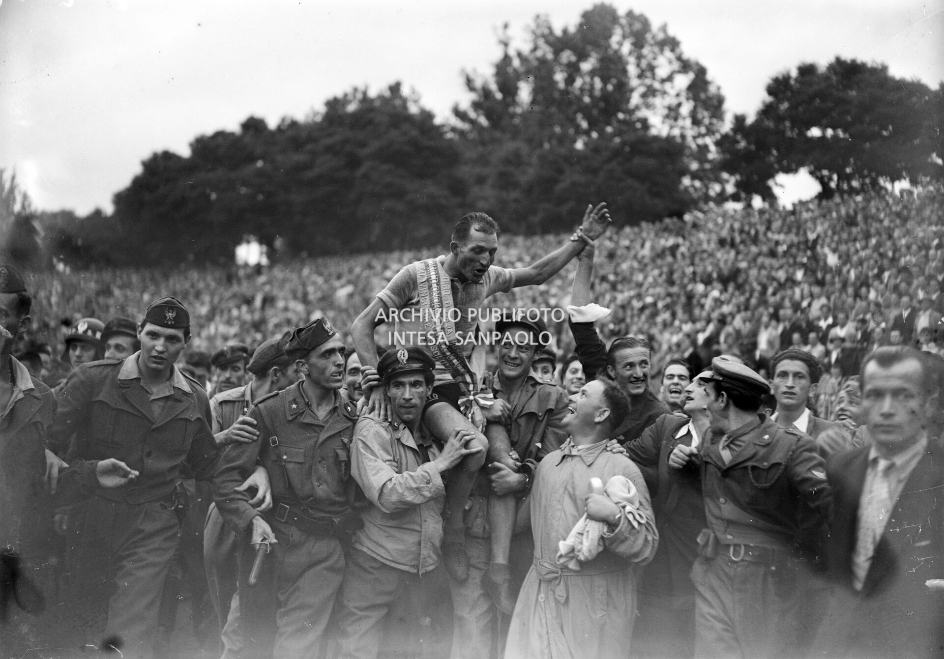 Gino Bartali, con la fascia di "vincitore assoluto", viene portato in trionfo dai suoi sostenitori all'Arena di Milano dove si è appena concluso il 29° Giro d'Italia