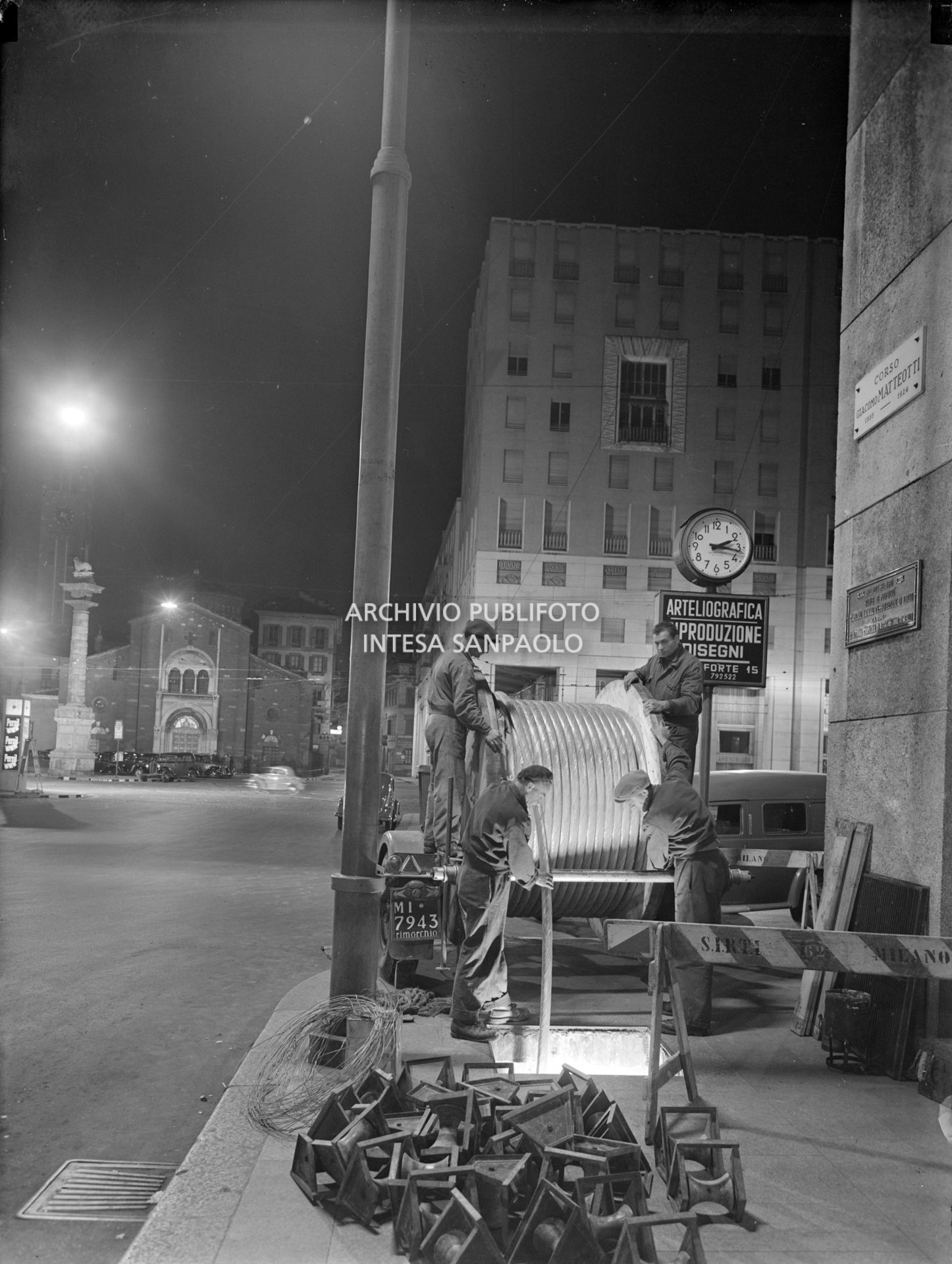 Operai della SIRTI (Società Italiana Reti Telefoniche Interurbane) posano,  di notte, cavi coassiali in corso Matteotti a Milano. Sullo sfondo piazza San Babila e l'omonima basilica