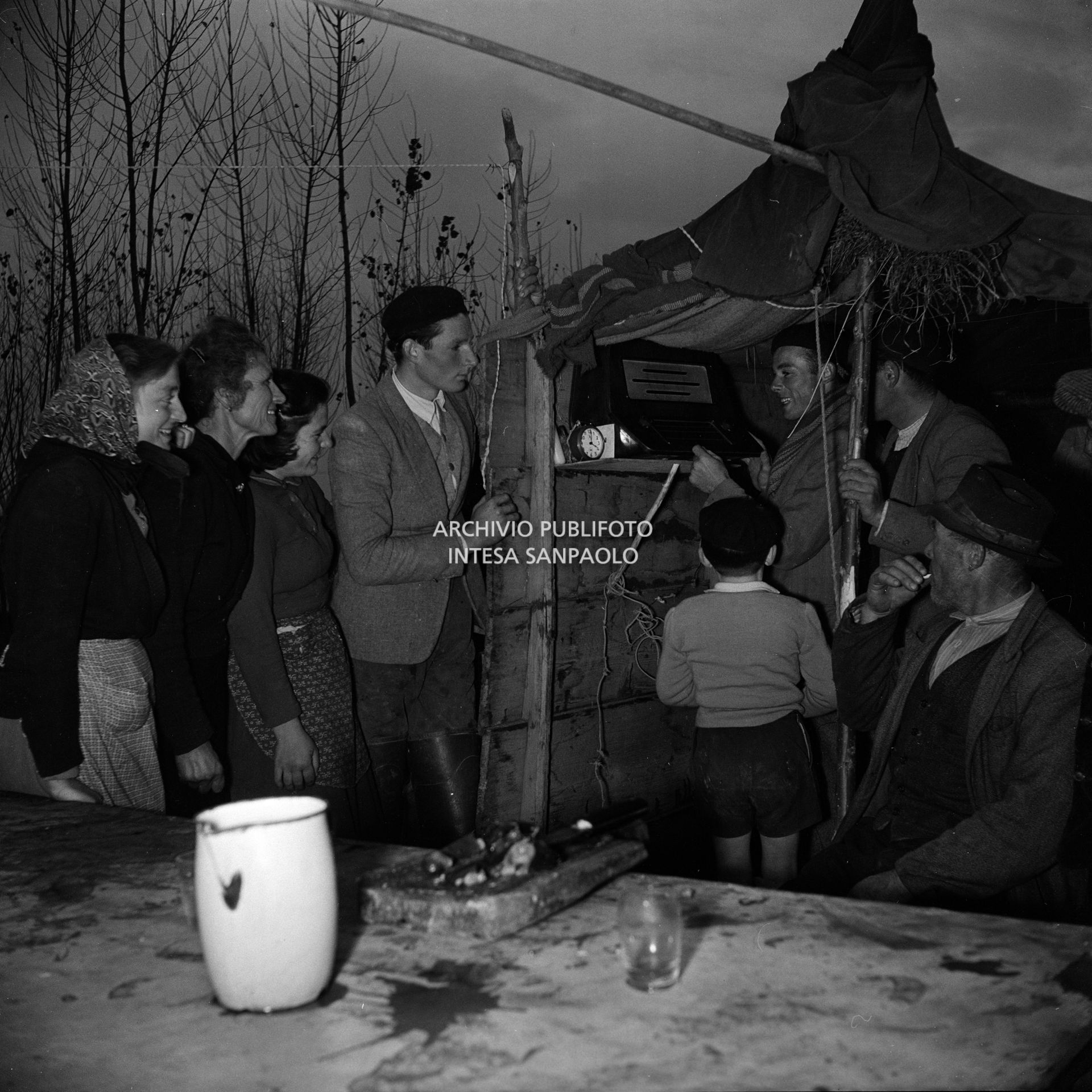 Un gruppo di alluvionati ascolta la radio in un accampamento di fortuna a Bosaro, nei giorni dell'alluvione del Polesine