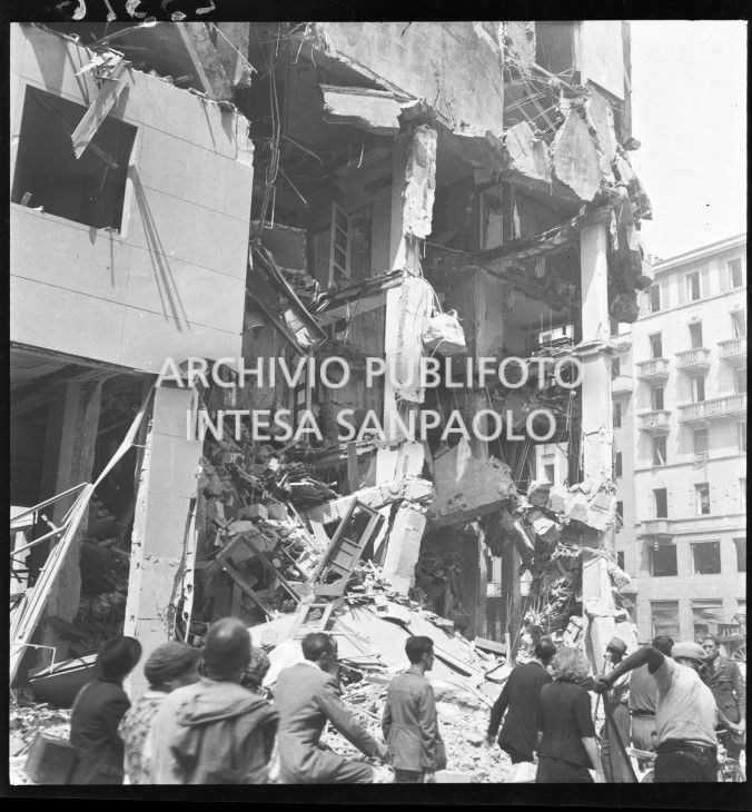 Passanti in via Torino all'angolo con piazza Santa Maria Beltrade, a Milano, davanti a un edificio sventrato dai bombardamenti