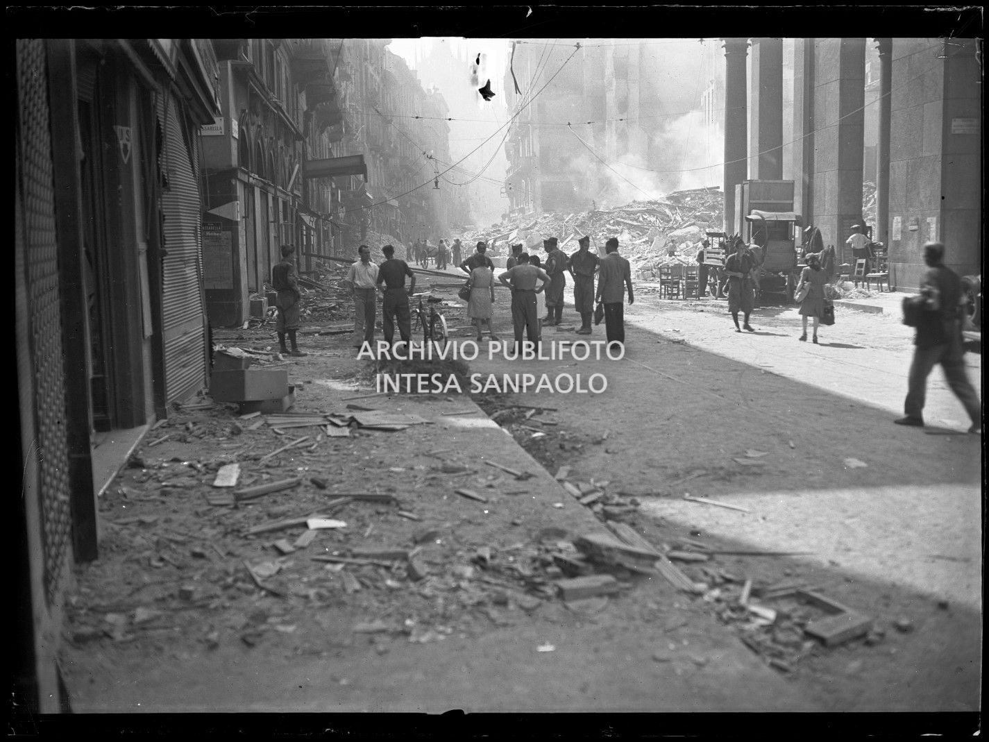 Militari e civili in corso Vittorio Emanuele II, verso piazza San Carlo, a Milano, all'indomani dei bombardamenti: la strada è ingombra delle macerie degli edifici distrutti o gravemente danneggiati durante gli attacchi aerei