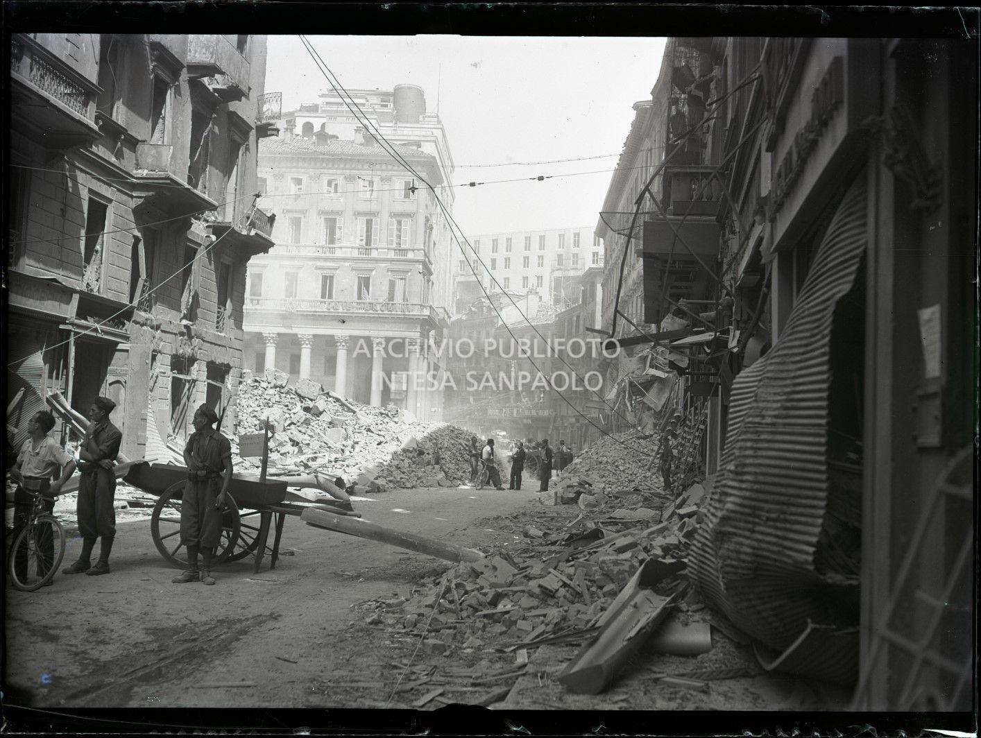 Corso Vittorio Emanuele II verso piazza San Carlo a Milano all'indomani dei bombardamenti: militari e civili osservano i danni causati dagli attacchi aerei che hanno distrutto o gravemente danneggiato gli edifici le cui macerie ingombrano la strada