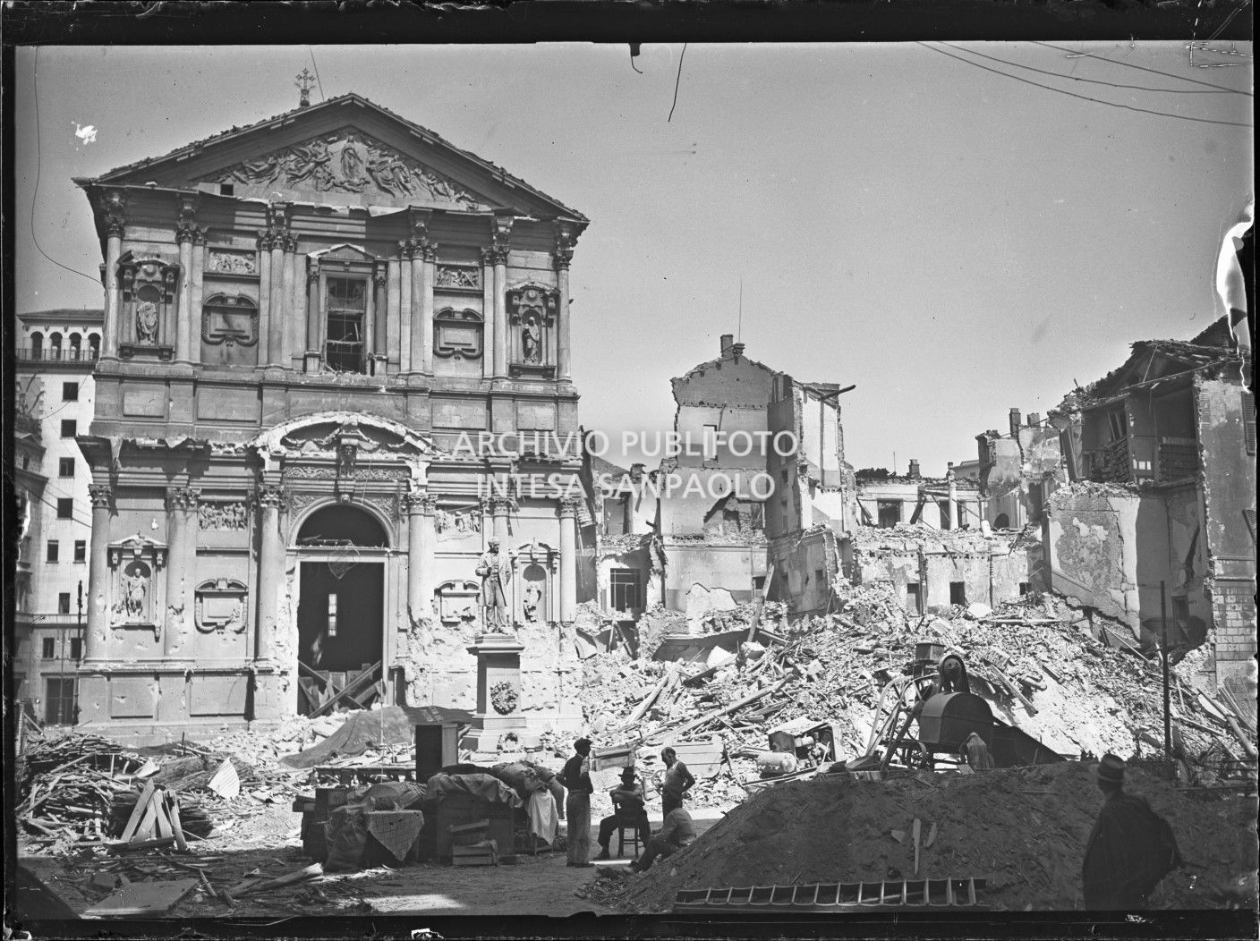 Chiesa di San Fedele a Milano gravemente danneggiata dai bombardamenti; sulla destra l'edificio che ospitava la questura della città, completamente distrutto; davanti alla chiesa il monumento a Alessandro Manzoni intatto