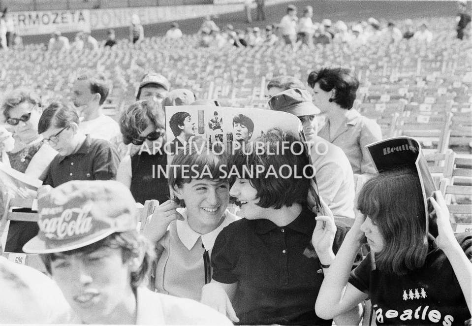Tre ragazze si riparano dal sole, al Vigorelli di Milano, con il programma del concerto dei Beatles in attesa che questo abbia inizio