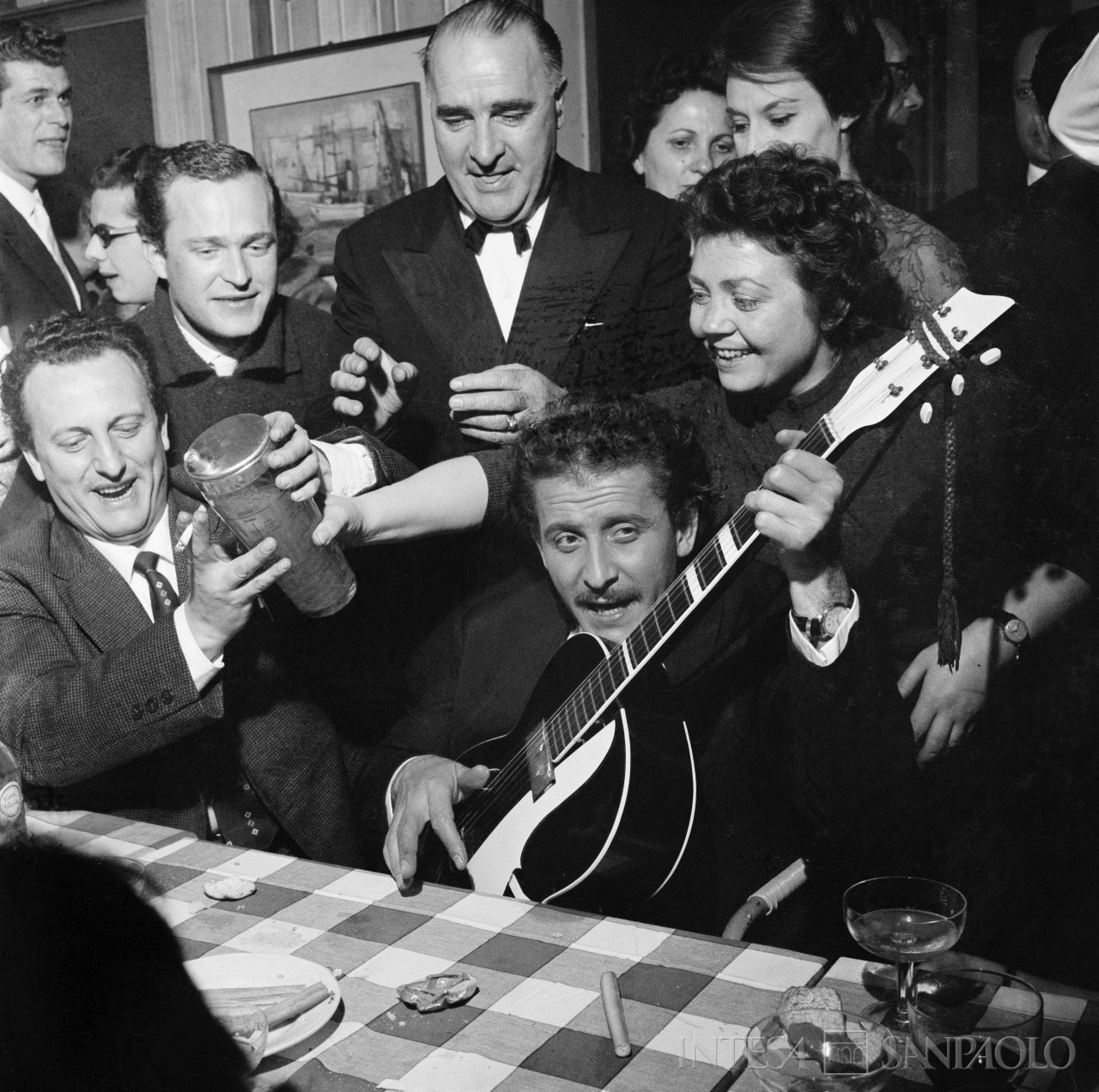 Domenico Modugno, con la chitarra, festeggia con amici, al ristorante, il Festival di Sanremo appena vinto insieme a Johnny Dorelli con la canzone "Piove"