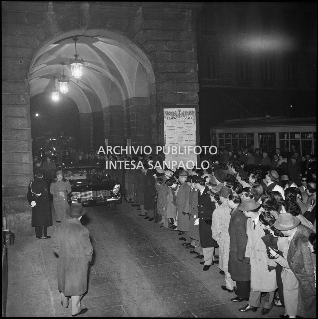 Folla di curiosi assiepata a ridosso della galleria delle carrozze del Teatro alla Scala, in occasione della serata inaugurale della stagione lirica 1957-1958 con l'opera  "Un ballo in maschera", di Giuseppe Verdi, diretta da Gianandrea Gavazzeni, con la regia di Margherita Wallmann