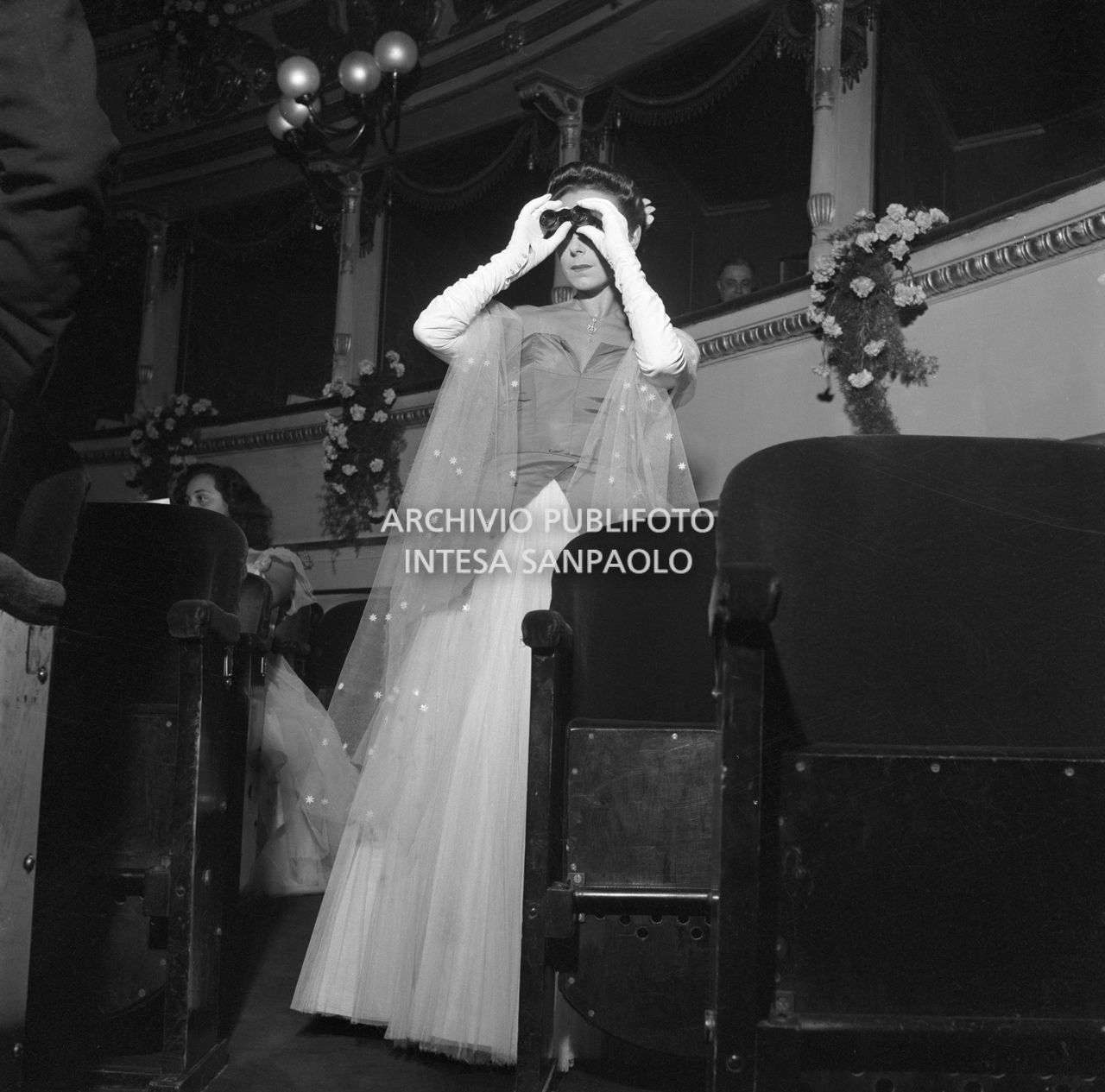 Una spettatrice nella platea del Teatro alla Scala, con un binocolo da teatro, in occasione della serata inaugurale della stagione lirica 1951-1952 con l'opera "I vespri siciliani" di Giuseppe Verdi, diretta da Victor de Sabata, con la regia di Herbert Graf