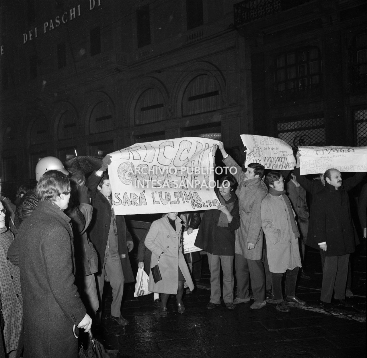 Contestatori del Movimento studentesco mostrano uno striscione con la scritta: "Ricchi godete! Sarà l'ultima volta", fuori dal Teatro alla Scala la sera dell'inaugurazione della stagione lirica 1968-1969, nel corso della quale lanciarono uova e vernice contro il pubblico in entrata