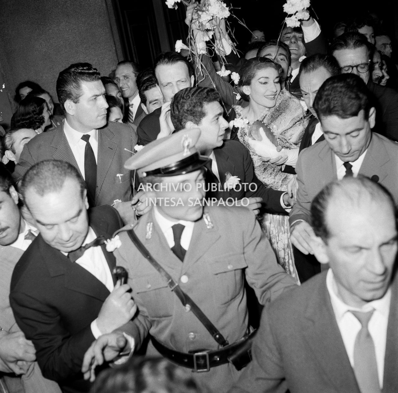 Maria Callas uscita dal Teatro alla Scala, dopo aver interpretato l'opera "Il pirata" di Vincenzo Bellini, si fa strada tra due ali di ammiratori entusiasti che le lanciano fiori