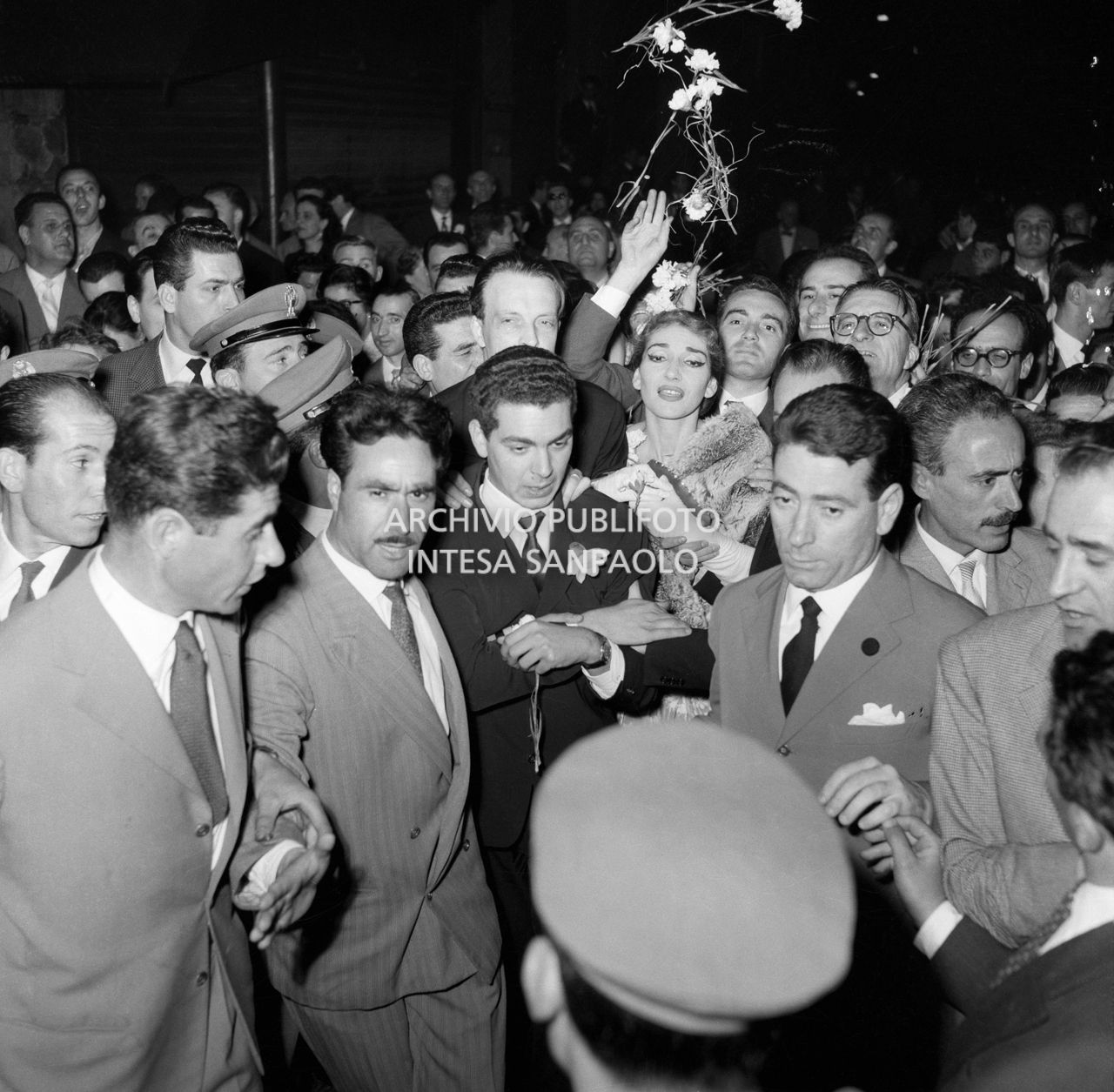Maria Callas uscita dal Teatro alla Scala, dopo aver interpretato l'opera "Il pirata" di Vincenzo Bellini, si fa strada tra due ali di ammiratori entusiasti che le lanciano fiori