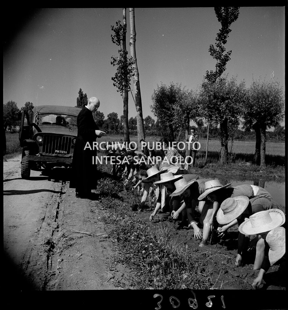 Don Balduzzi speaks to the rice-weeders bent down as they work near Vigevano