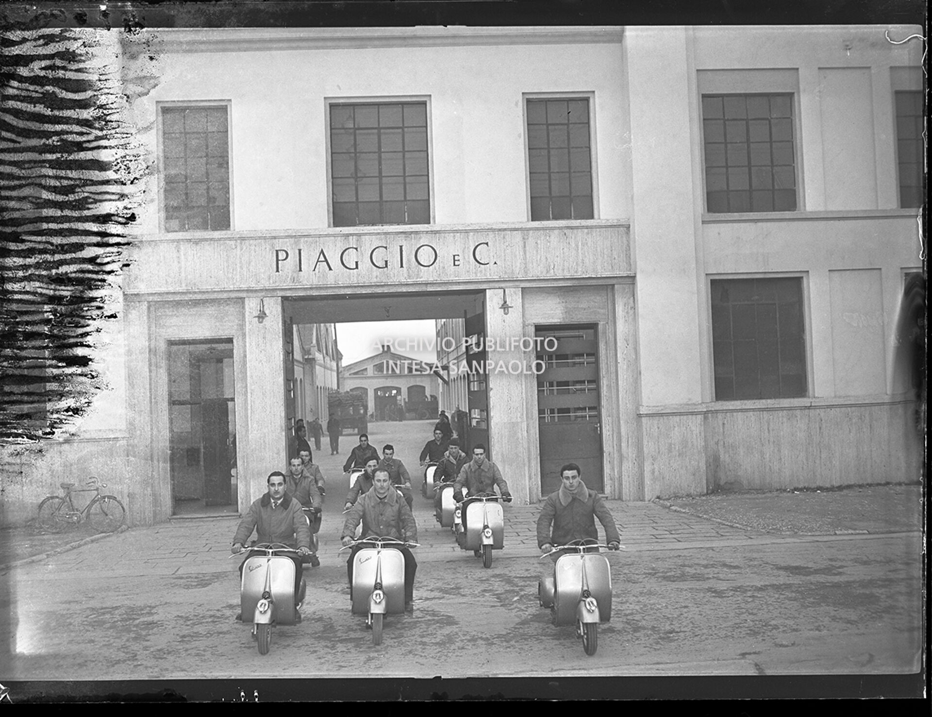Operai della Piaggio & C. in sella alla Vespa davanti all'ingresso dello stabilimento a Pontedera
