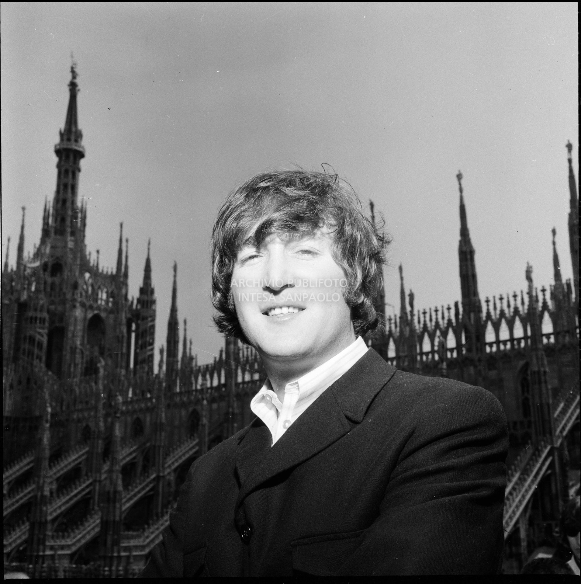 John Lennon ritratto sulla terrazza del Grand Hotel Duomo a Milano; sullo sfondo le guglie della cattedrale