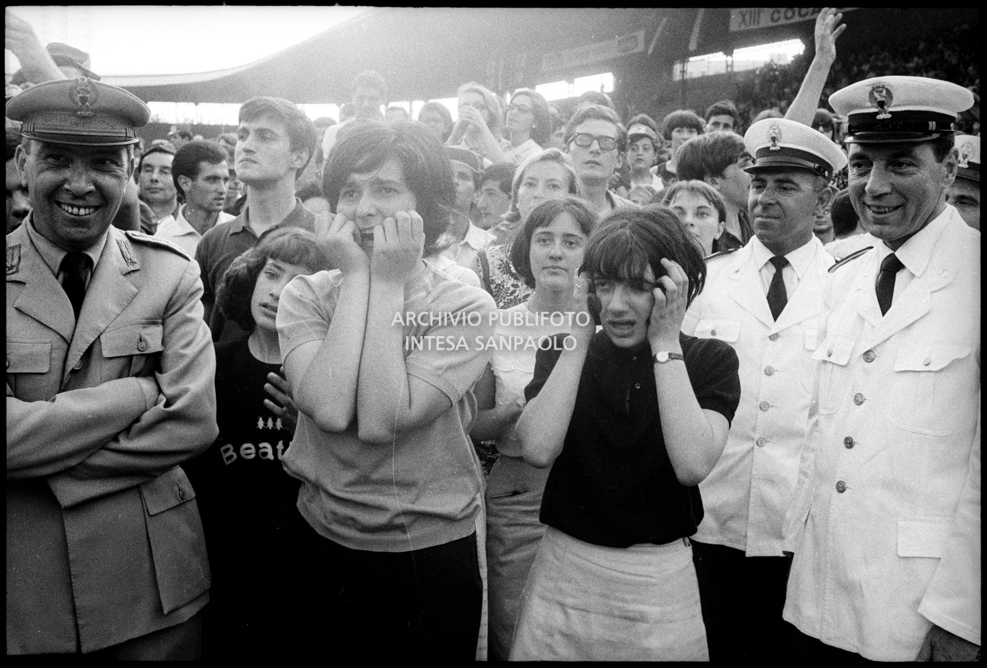 Ragazze, tra il pubblico al concerto pomeridiano dei Beatles al Vigorelli di Milano, urlano per l'entusiasmo; i poliziotti della sicurezza sorridono divertiti